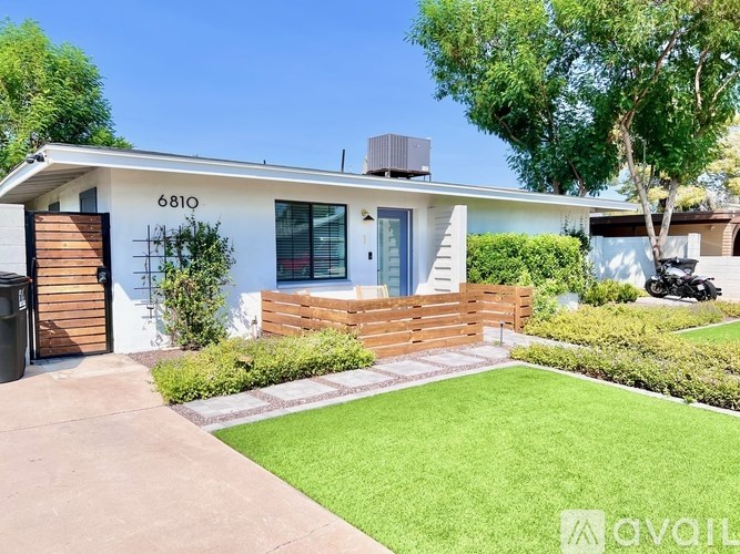 A house with the number 6810 on it has a white wall and a black trash can.