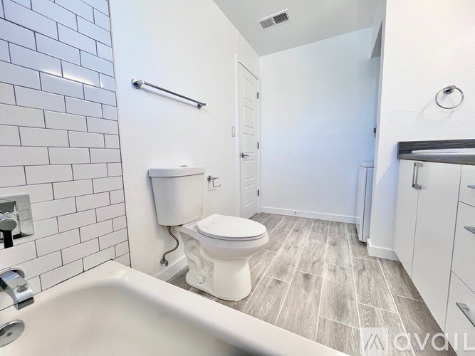 A white toilet is in a bathroom with a white tub and a white sink.