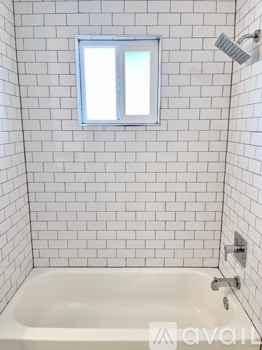 A white tiled bathroom with a window and a bathtub.