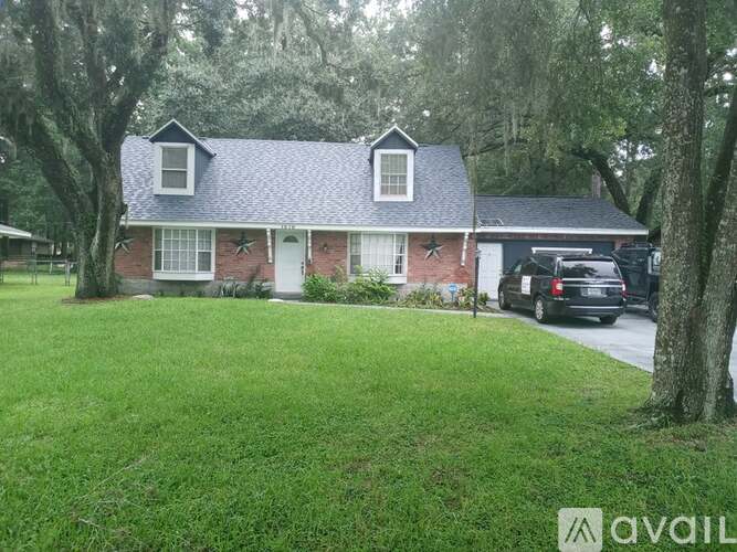 A house with a brick facade and a white door is surrounded by a grassy lawn and trees.