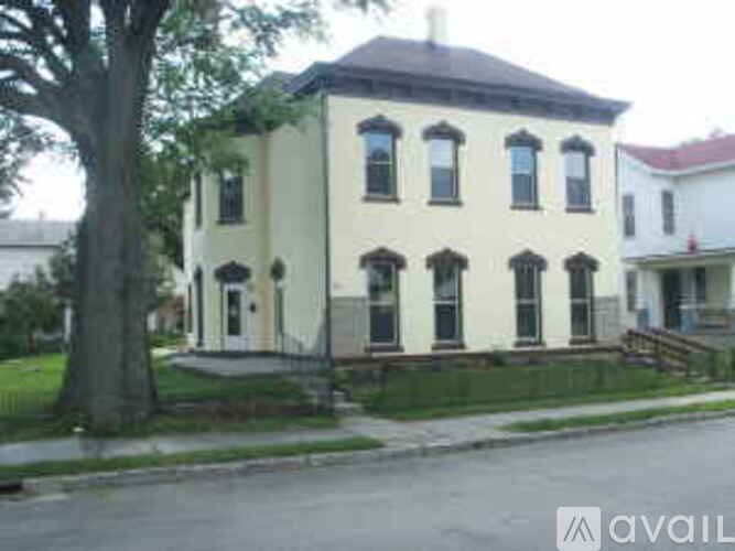 A white two-story house with a black roof and a tree in front.