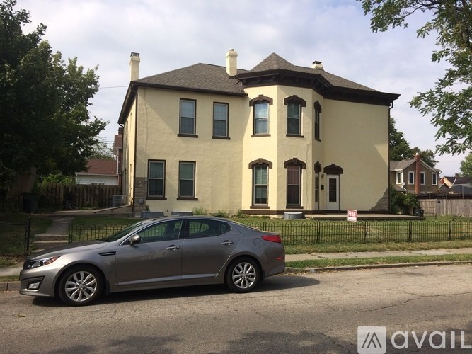 A silver car is parked in front of a two-story house.