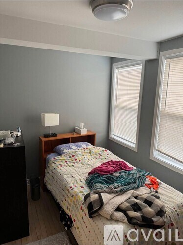 A bedroom with a bed covered in blankets and a nightstand with a lamp.