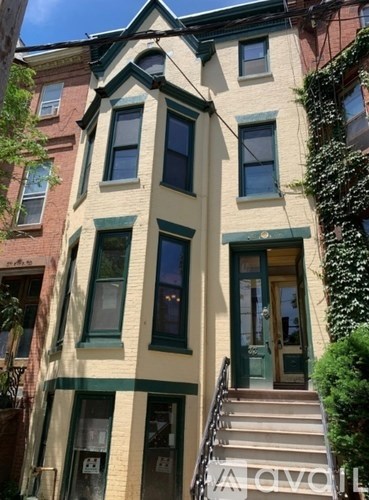 A yellow building with green trim and a staircase leading to the front door.