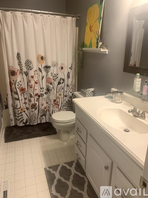 A bathroom with a floral shower curtain and a sink with a mirror above it.