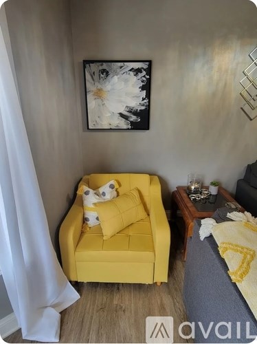 A yellow chair with a pillow and a picture on the wall.