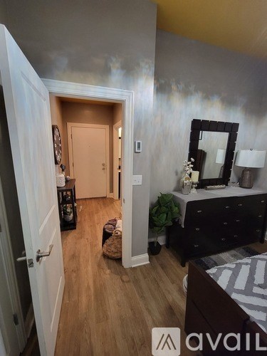 A bedroom with a bed, dresser, mirror, and a doorway leading to another room.