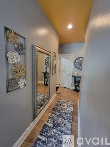 A hallway with a mirror, a rug, and a clock on the wall.