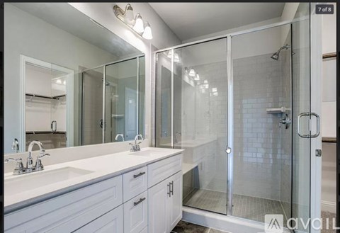 A bathroom with a walk-in shower and double sinks.
