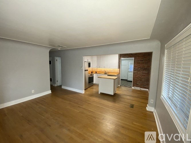 A room with wooden floors and white walls, with a kitchenette in the background.