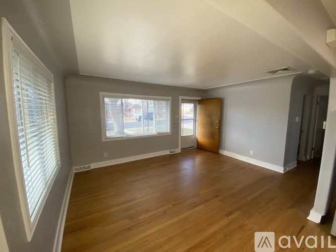 A room with wooden floors and a large window with blinds.