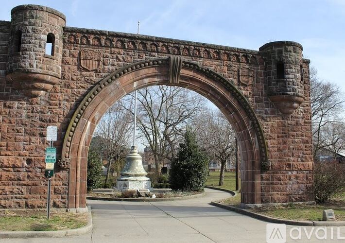 A stone archway leads to a park with a statue in the distance.