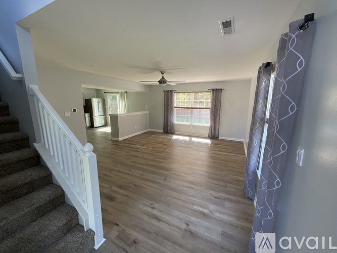 A living room with a staircase on the left and a window with curtains on the right.