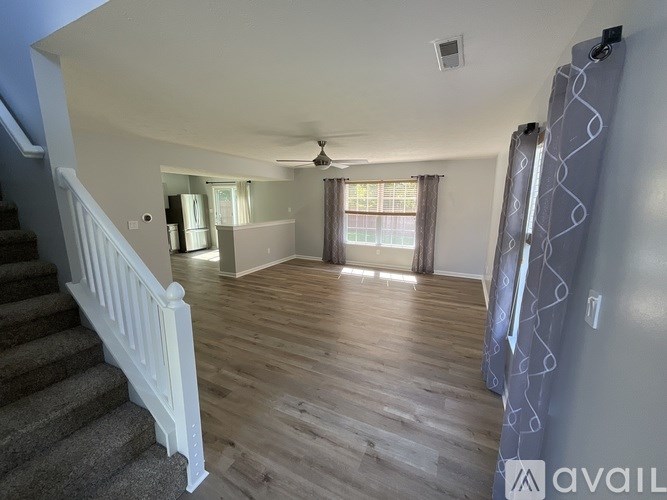 A living room with a staircase on the left and a window with curtains on the right.