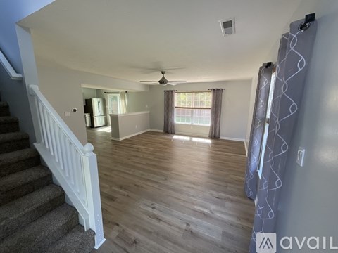 A living room with a staircase on the left and a window with curtains on the right.