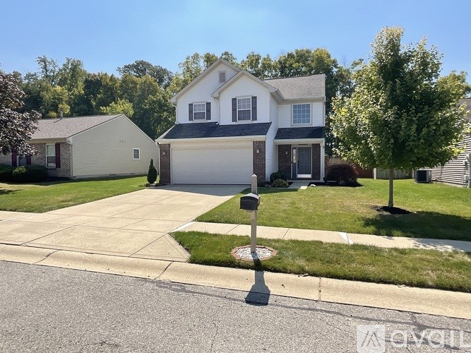 A white house with a grey roof and a garage door is in front of a tree.