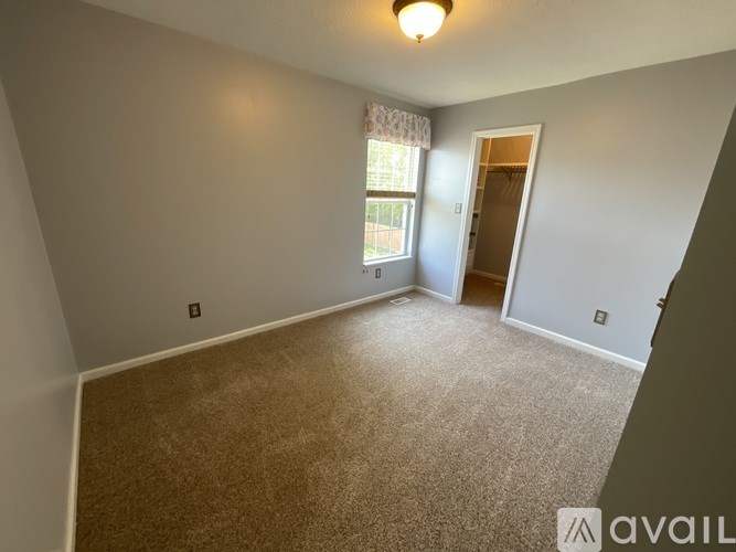 A room with a carpeted floor and a window with a white curtain.