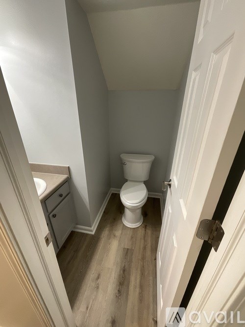 A small, white toilet in a small bathroom with wood flooring.