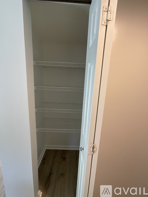A white door with a handle is open to a room with a white wall and a wooden floor.