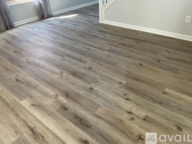 A room with a wooden floor and a window with curtains.