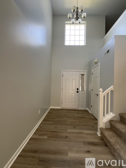 A hallway with a chandelier, a staircase, and a door.