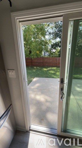 A white door with a glass window is open to a backyard.