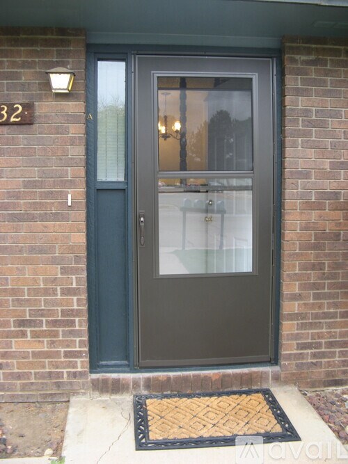 A grey door with a glass window and a black mat in front of it.