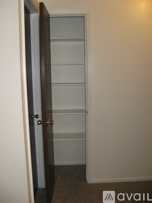 A brown door with a gold handle is open to a white hallway.