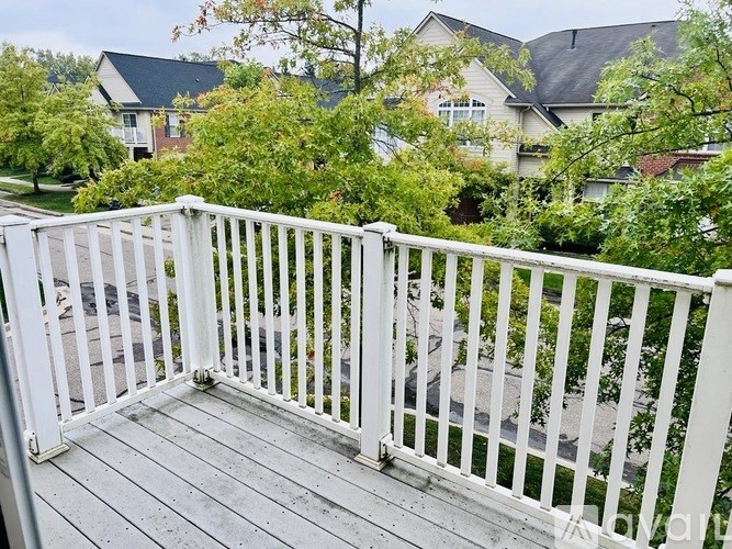 A white railing on a wooden deck overlooks a residential street.