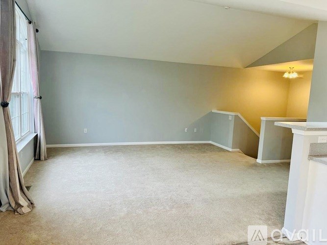 A spacious room with a carpeted floor and a window with curtains.