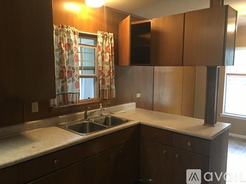 A kitchen with wooden cabinets and a window with curtains.