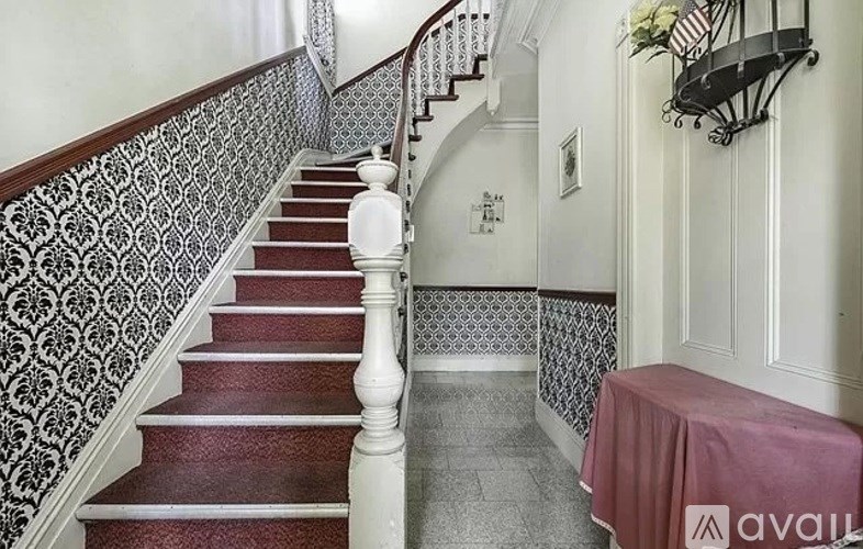 A staircase with a red carpeted runner and a black and white patterned wallpaper on the wall.