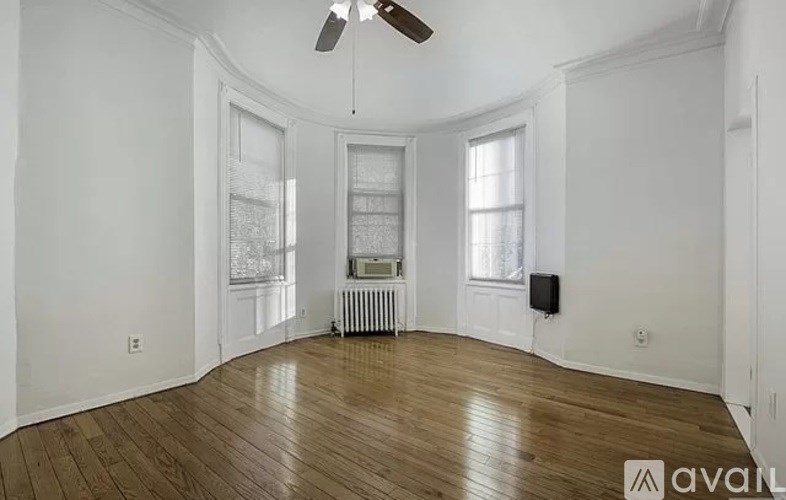 A room with wooden floors and white walls, featuring a ceiling fan and a window.
