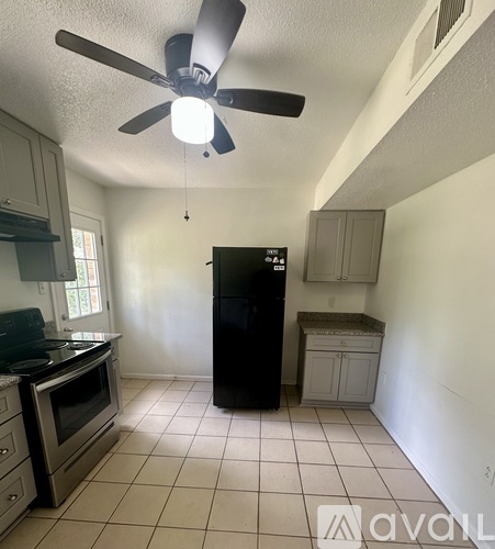 A kitchen with a black fridge and a ceiling fan.