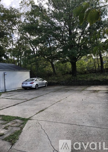 A car is parked in a driveway with a garage door and trees in the background.