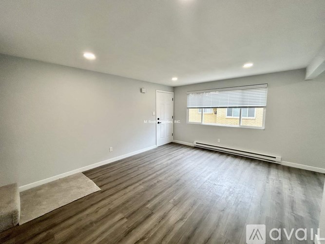 A spacious room with wooden flooring and a window with blinds.
