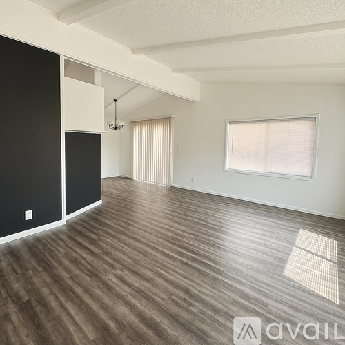 A spacious room with wooden flooring and a window with blinds.
