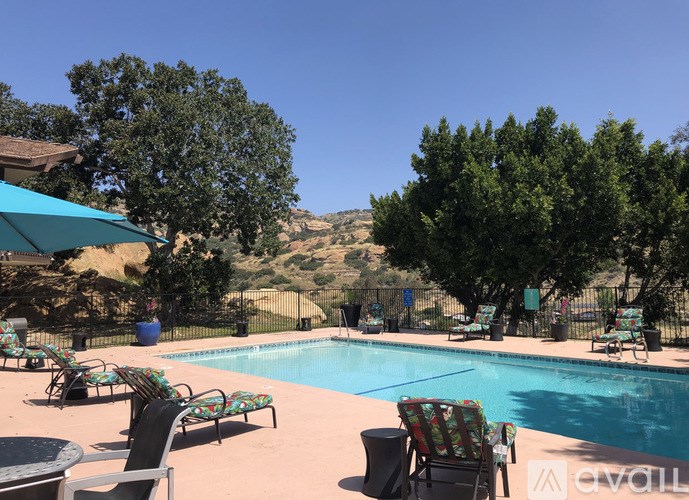 A pool surrounded by chairs and trees.