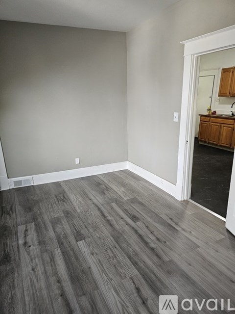 A room with wooden flooring and a white door leading to a kitchen.