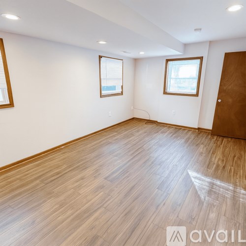 A room with wooden flooring and two windows.