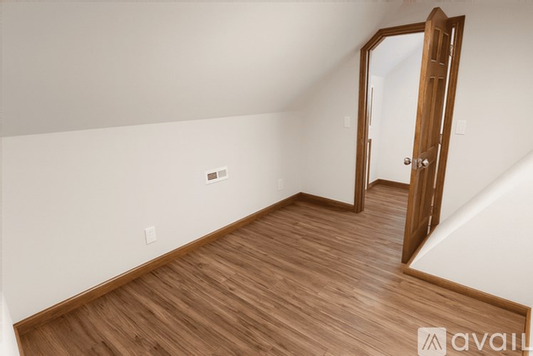 A room with wooden flooring and a door leading to another room.