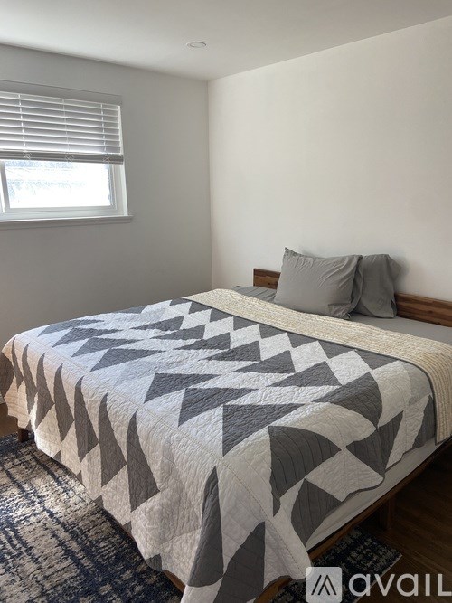 A bed with a grey and white comforter in a room with a window.