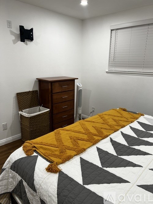 A bedroom with a bed, a dresser, and a trash can.