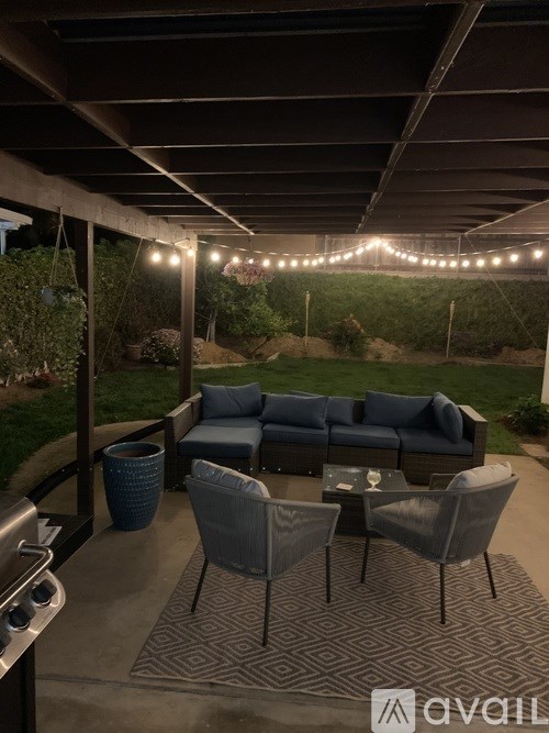 A patio with a grey couch, chairs and a table with a grill.