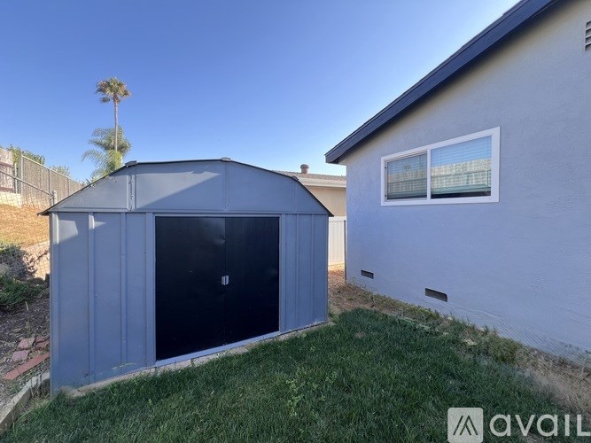 A blue shed is in front of a house.