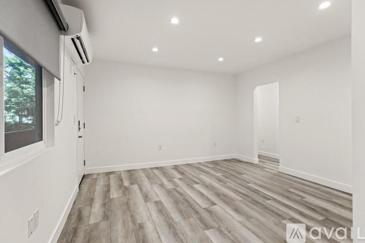 A spacious room with wooden flooring and a window on the left side.