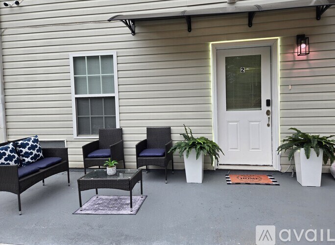 A patio with a white door, two chairs, a table, and two potted plants.