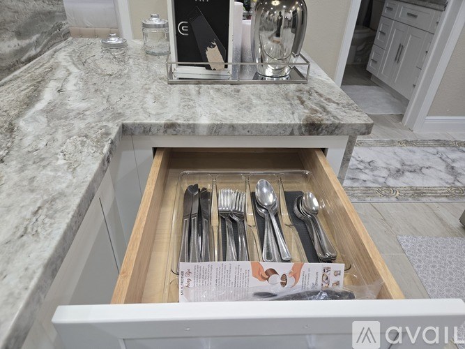 A drawer of silverware is open on a marble countertop.