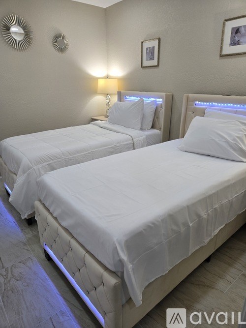 Two beds with white bedspreads and pillows are illuminated by blue LED lights.