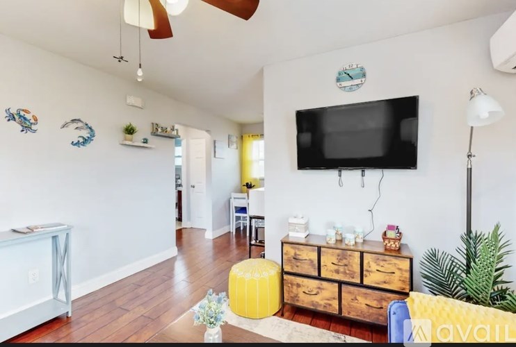 A living room with a TV, a yellow ottoman, and a wooden dresser.